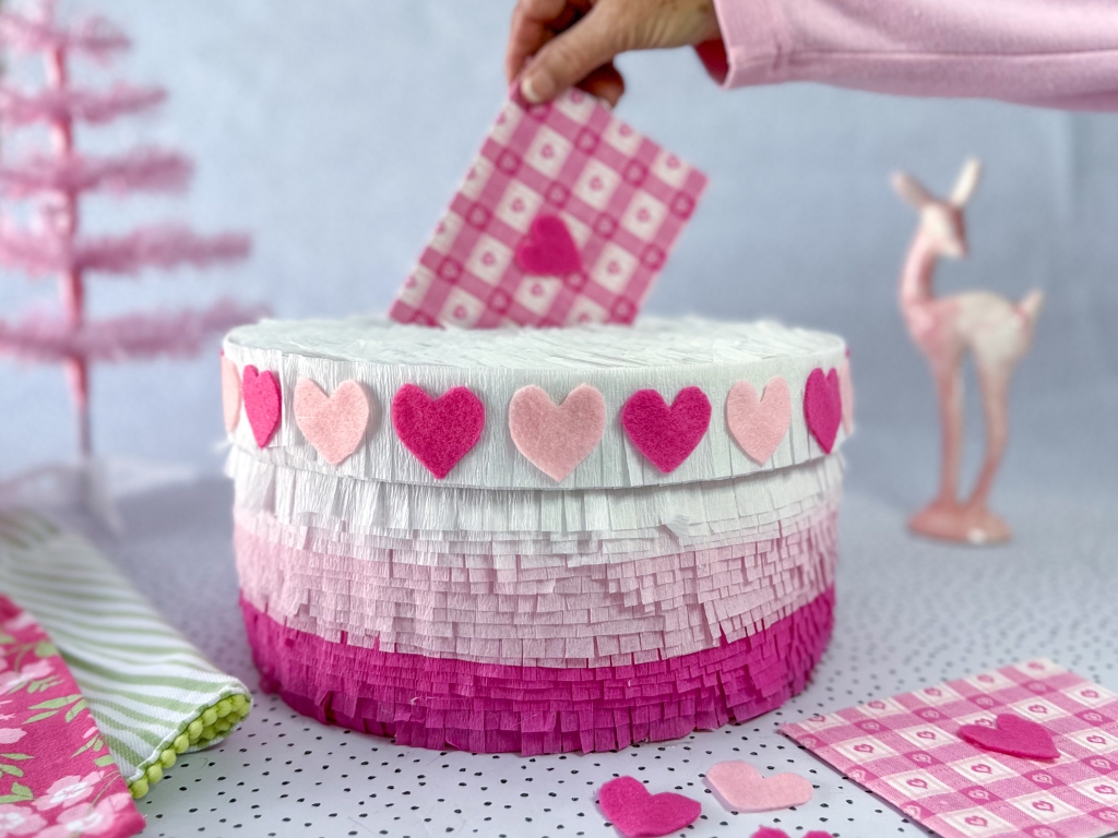 Finished Pink Ombre Cake Valentine Box with a hand inserting a Valentine card into the top slot