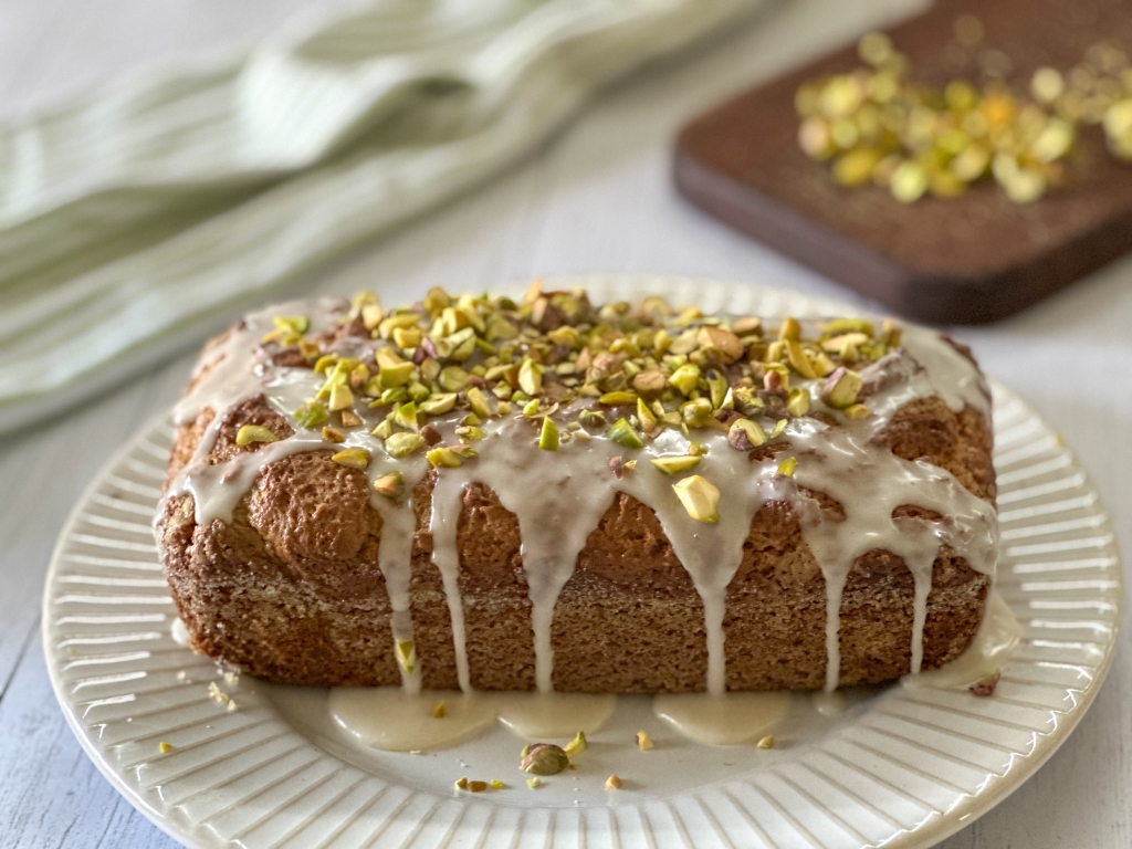 loaf of pistachio bread with glaze and topped with chopped pistachios
